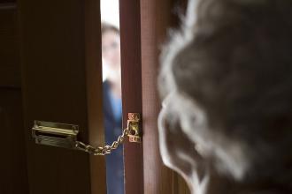 Eine Seniorin schaut durch einen Spalt einer kettengesicherten Tür
