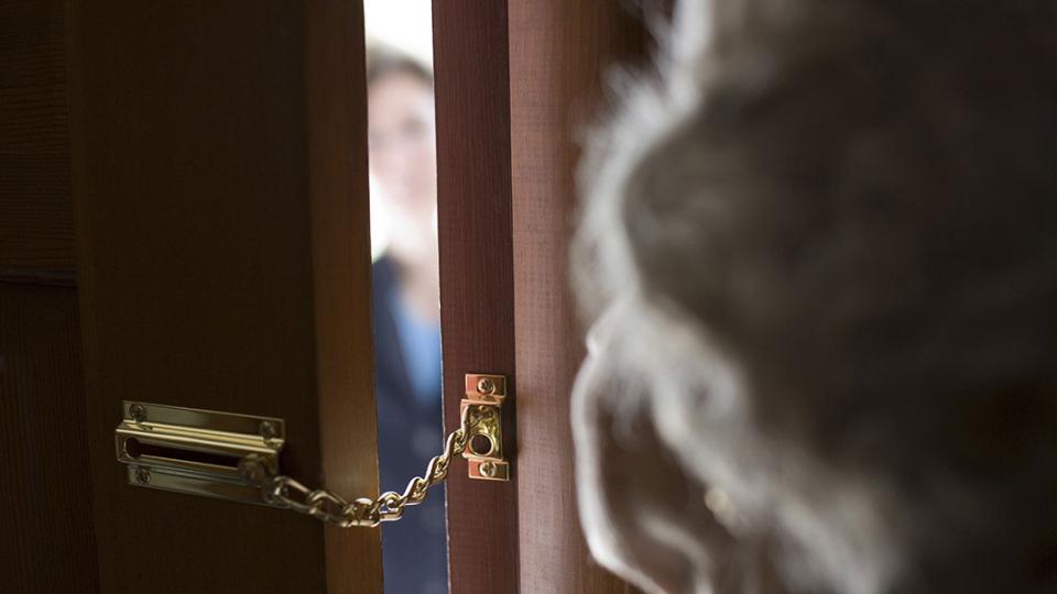 Eine Seniorin schaut durch einen Spalt einer kettengesicherten Tür