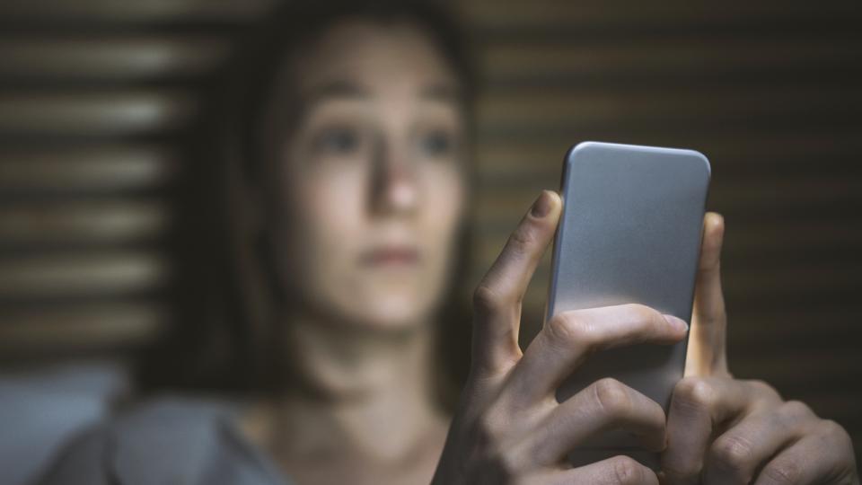 Besorgte Frau im dunklen Raum mit Handy in den Händen